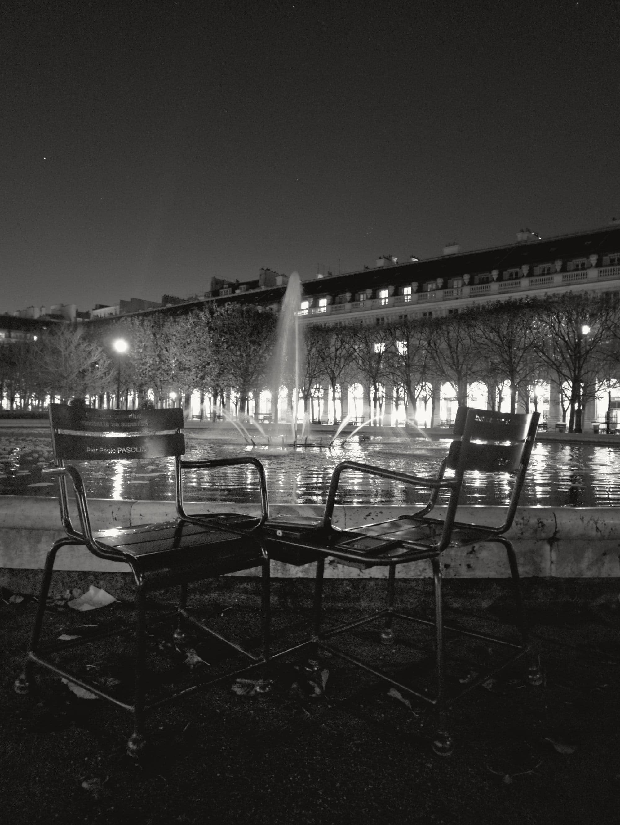 Two empty chairs beside a fountain at night
