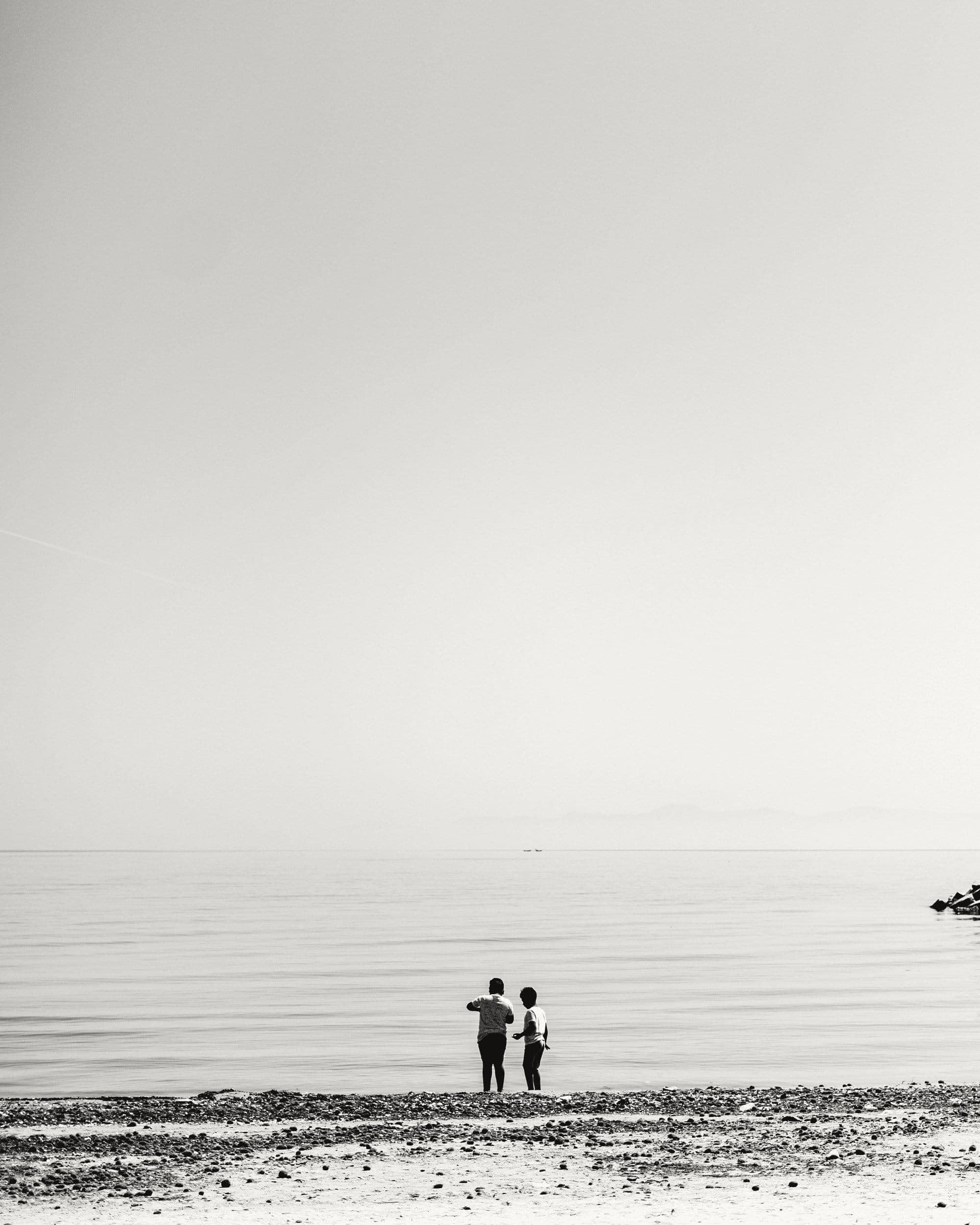 Two people standing at the water's edge on a quiet beach